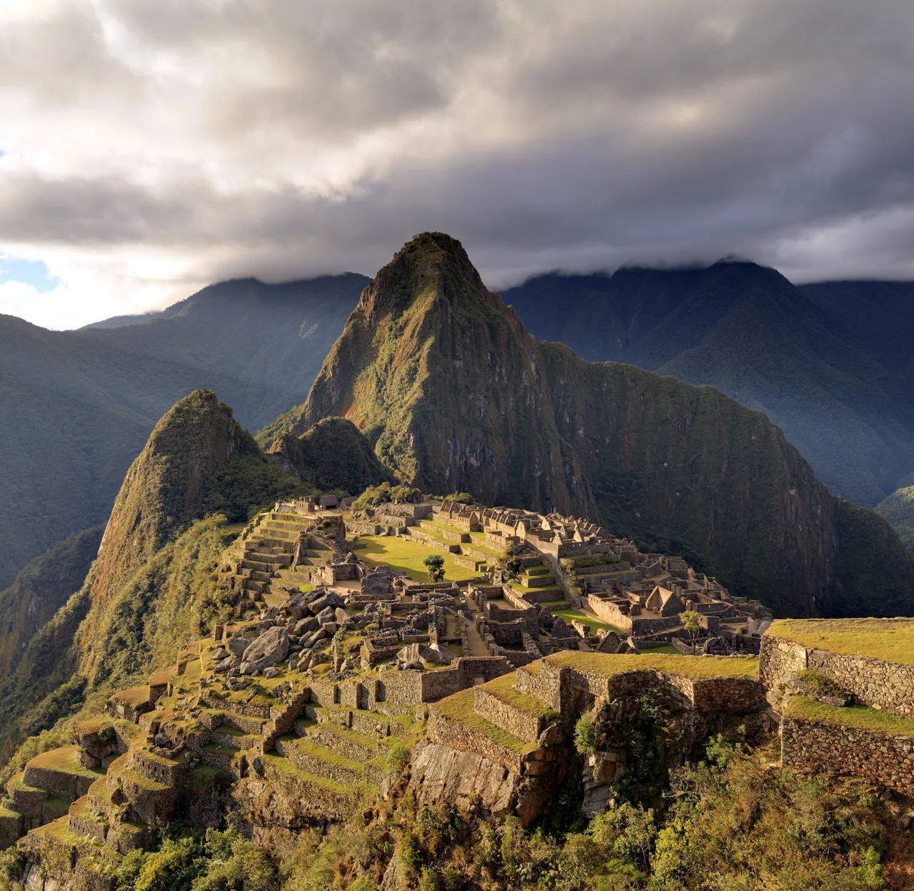 The stone buildings of Machu Picchu on the mountain ridge and the terraces stepping the slope; the Huayna Picchu peak behind