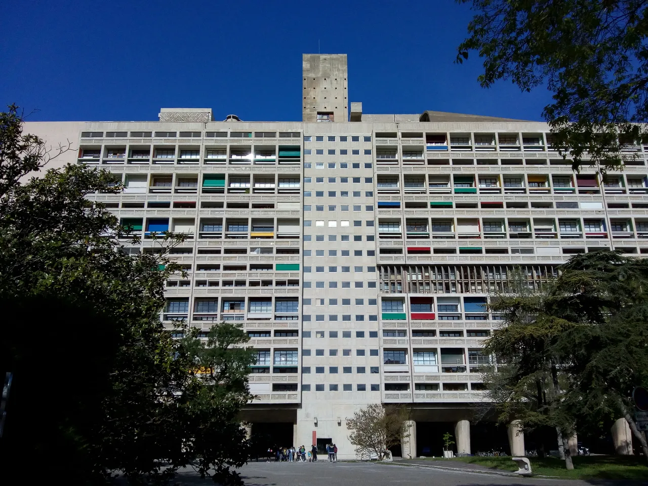 The bare reinforced-concrete façade of the Unité d'Habitation rising on pilotis, with coloured balconies