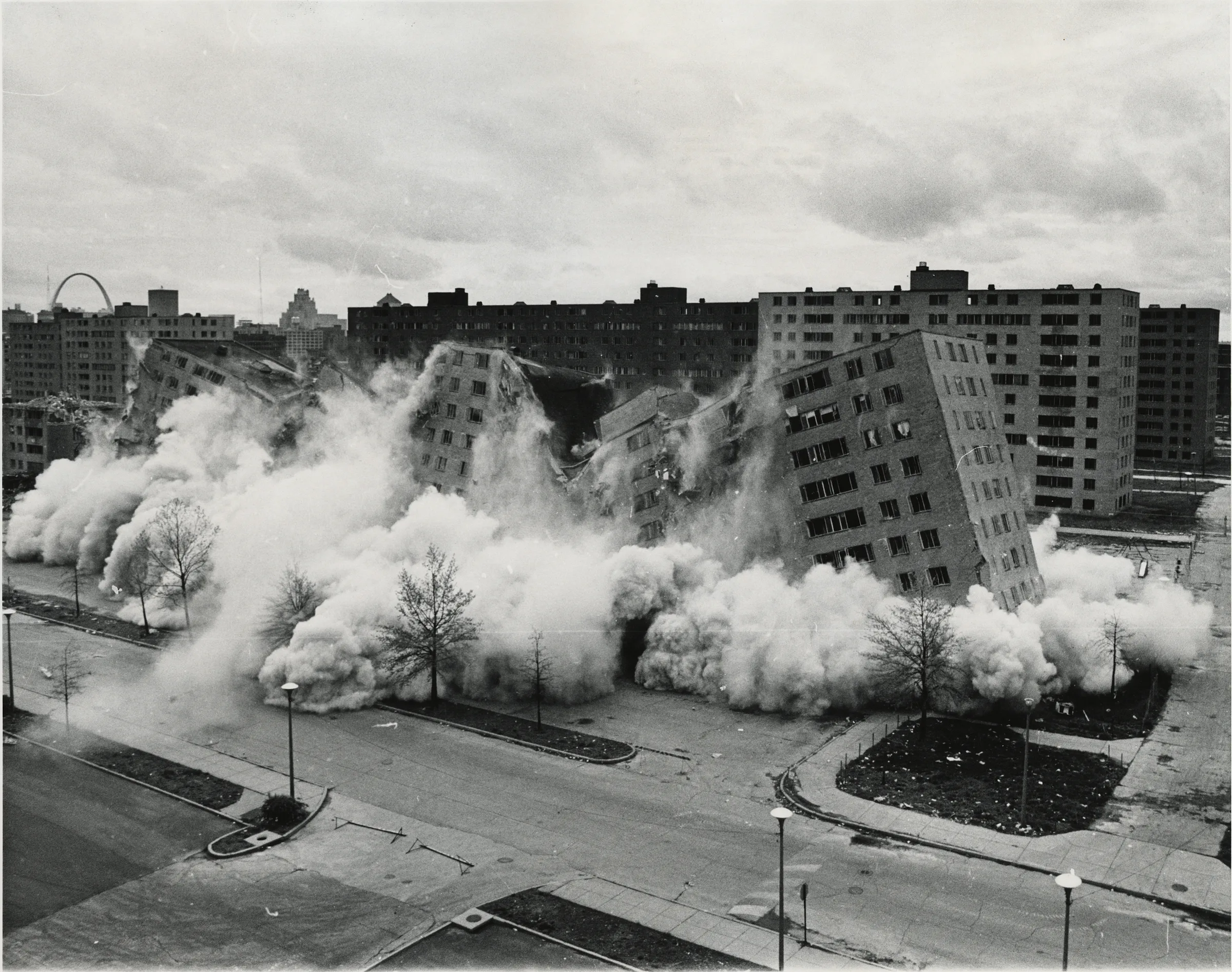 Pruitt-Igoe bloklarından birinin dinamitle çökmesi: toz bulutu içinde yana devrilen betonarme yapı