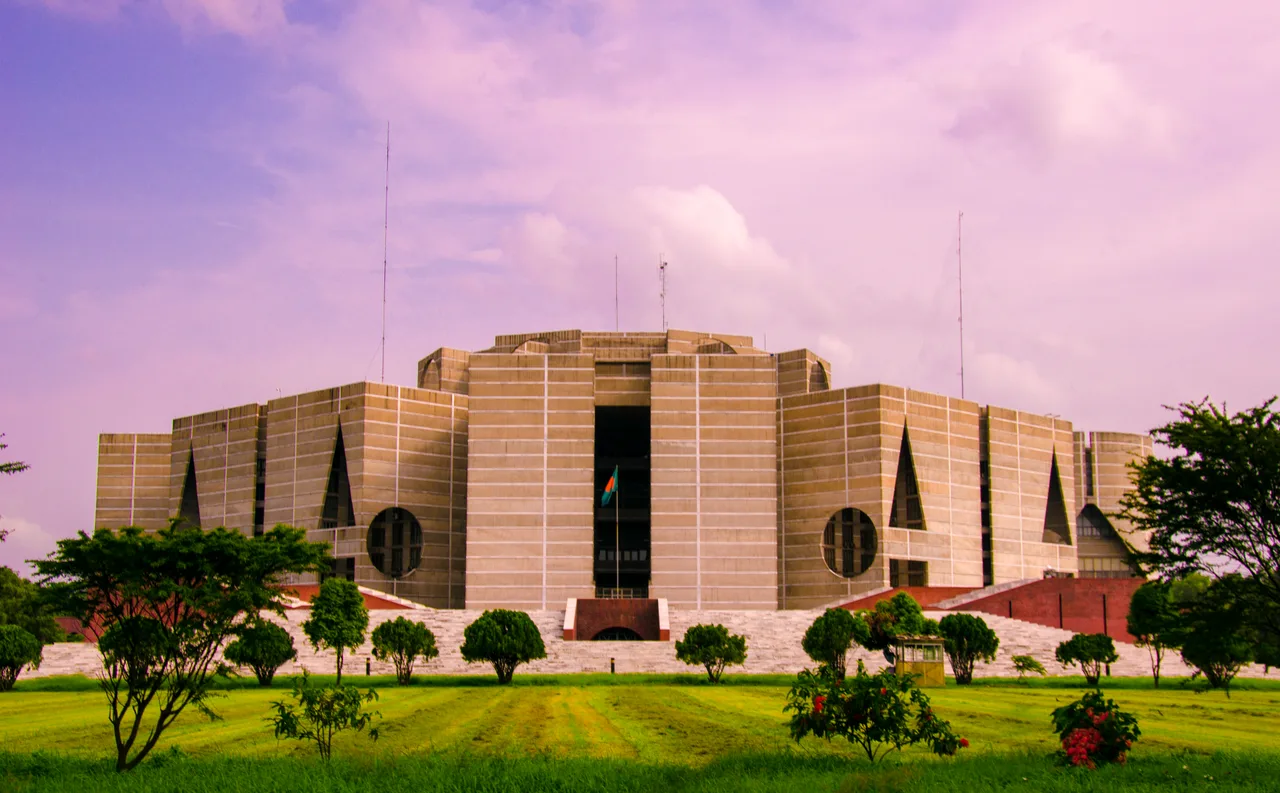 The monumental concrete outer shell of the Bangladesh National Parliament, pierced with giant circular and triangular openings, across the lake