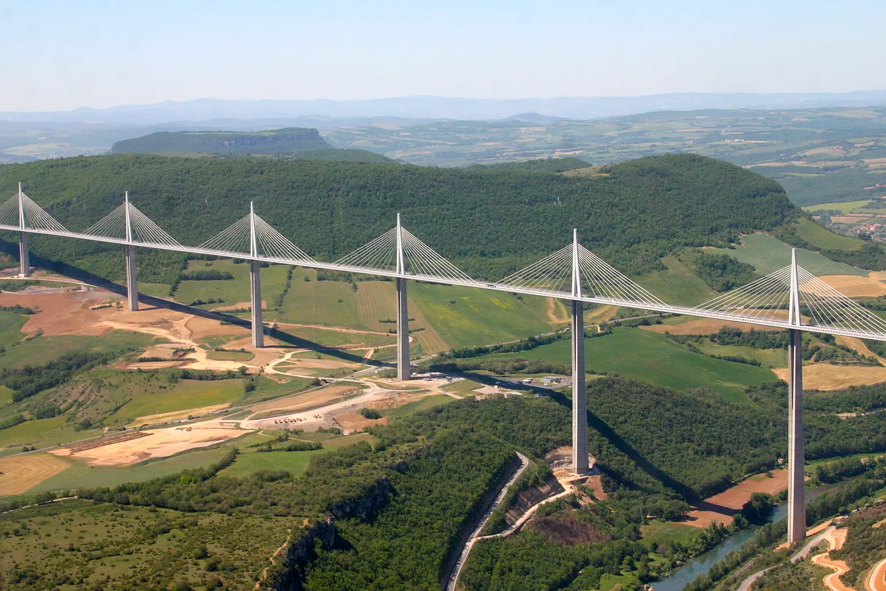 The steel deck of the Millau Viaduct crossing the deep Tarn valley, hung by cables from slender masts, with mist in the valley