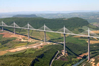 The steel deck of the Millau Viaduct crossing the deep Tarn valley, hung by cables from slender masts, with mist in the valley