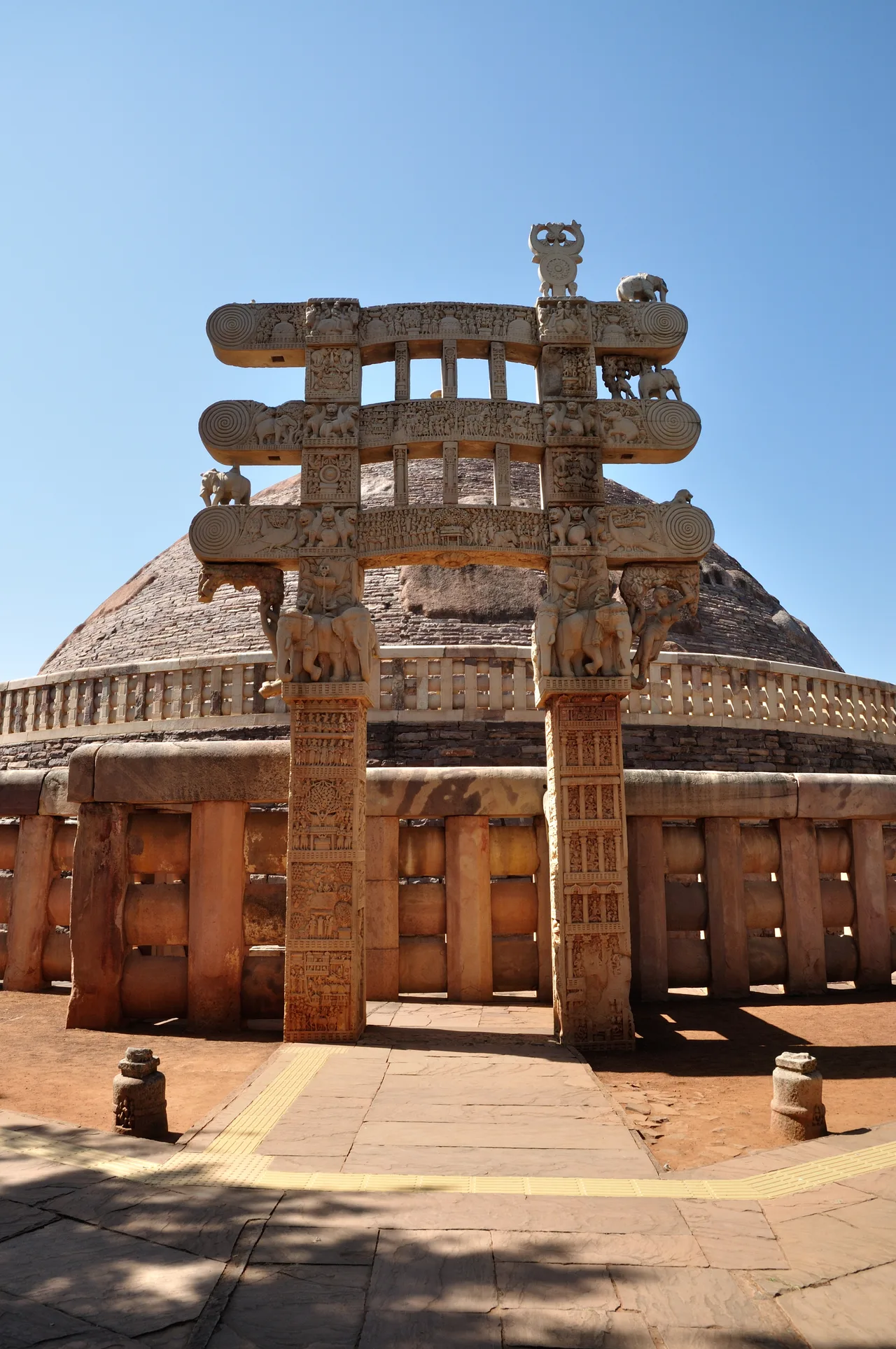 The east torana of the Great Stupa at Sanchi: a three-architrave stone ceremonial gateway carved with dense relief, with the hemispherical stupa rising behind