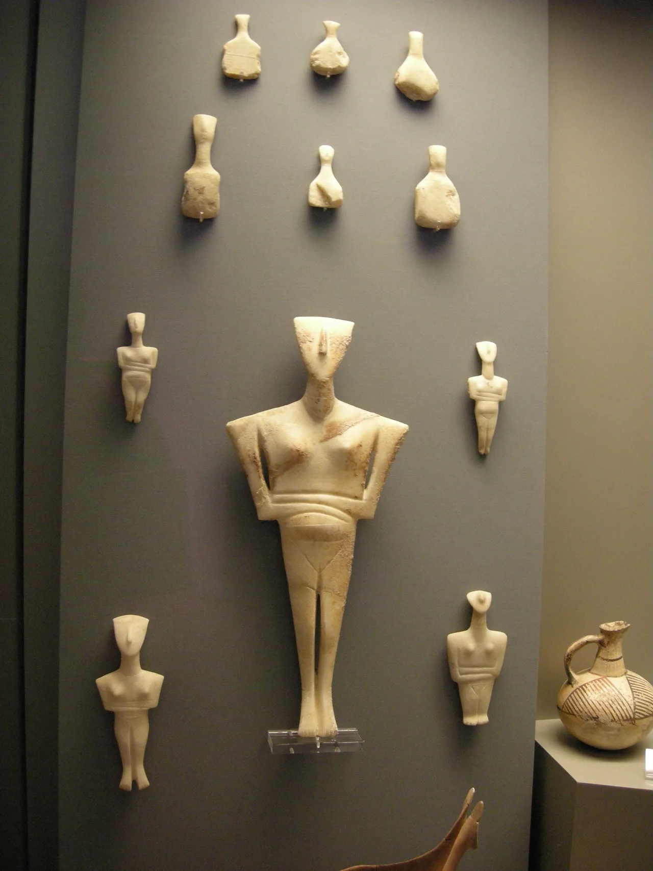 A Cycladic marble figurine: a slender abstracted female form, arms folded across the chest, head tilted slightly back