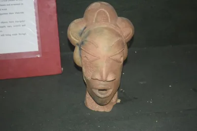 A terracotta human head: almond-shaped pierced eyes, elaborate coiffure and broad nose