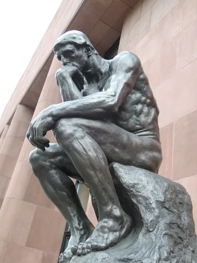 Rodin's The Thinker in bronze: a nude male figure hunched on its base, elbow on the opposite knee, every muscle tensed