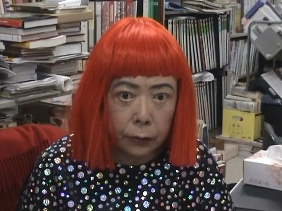 Photograph of Yayoi Kusama in 2005: the artist standing in a space carrying her own patterns
