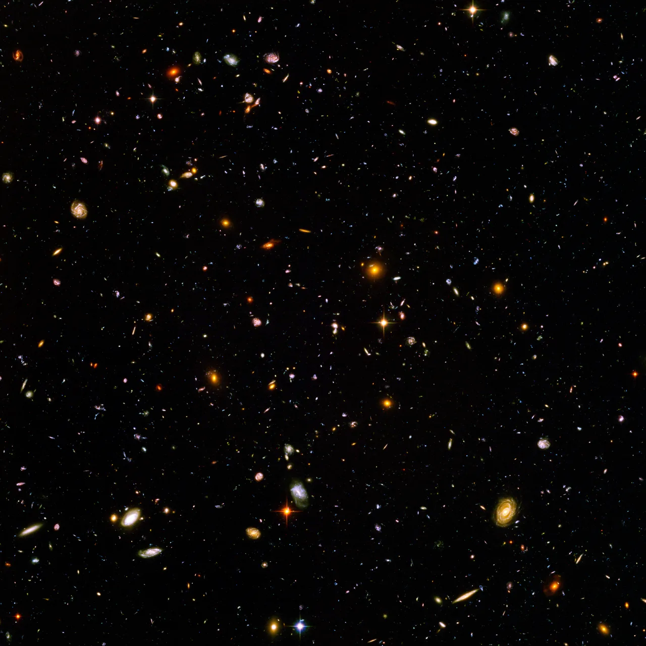 The Hubble Ultra-Deep Field — thousands of small galaxies in dark space: spirals, ellipticals, blurry smudges, ancient ultraviolet light shifted into the red