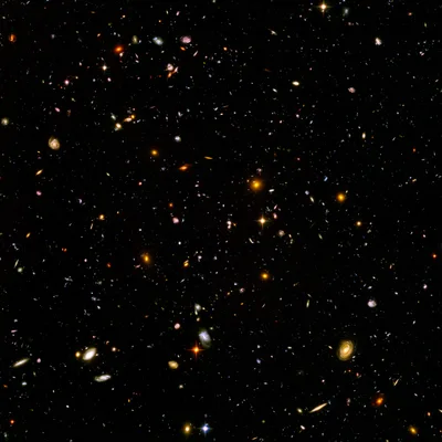 The Hubble Ultra-Deep Field — thousands of small galaxies in dark space: spirals, ellipticals, blurry smudges, ancient ultraviolet light shifted into the red