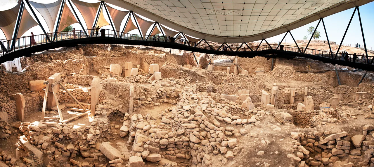 Göbeklitepe arkeolojik alanının panoramik görünümü; koruma çatısı altında dairesel yapı kompleksleri