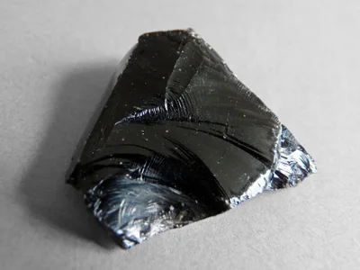 Close-up of glossy black obsidian: a smooth glassy surface with sharp fractured edges