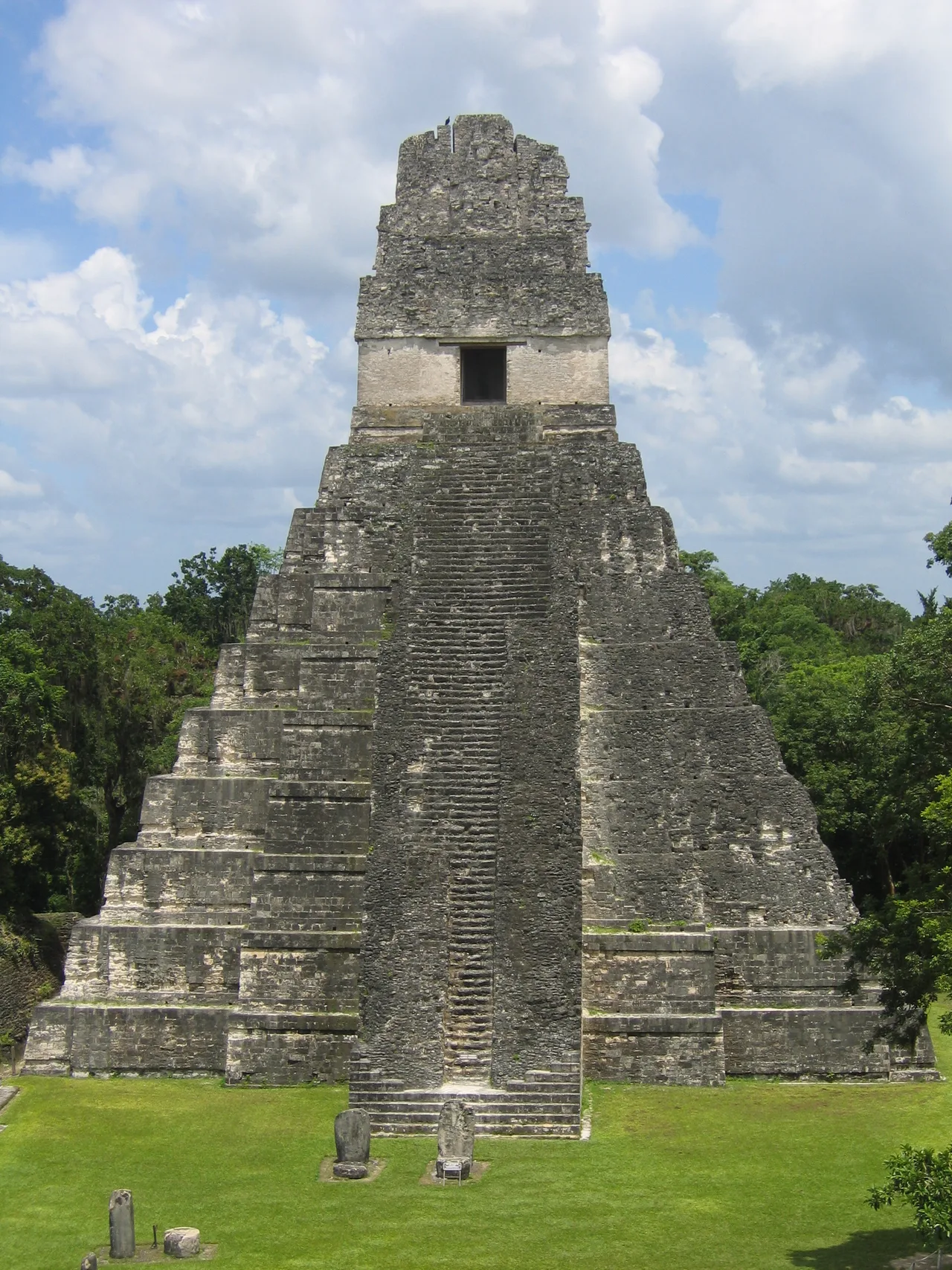 Front view of a nine-tiered Maya pyramid temple at Tikal with a steep staircase running up the centre and a roofed shrine at the summit