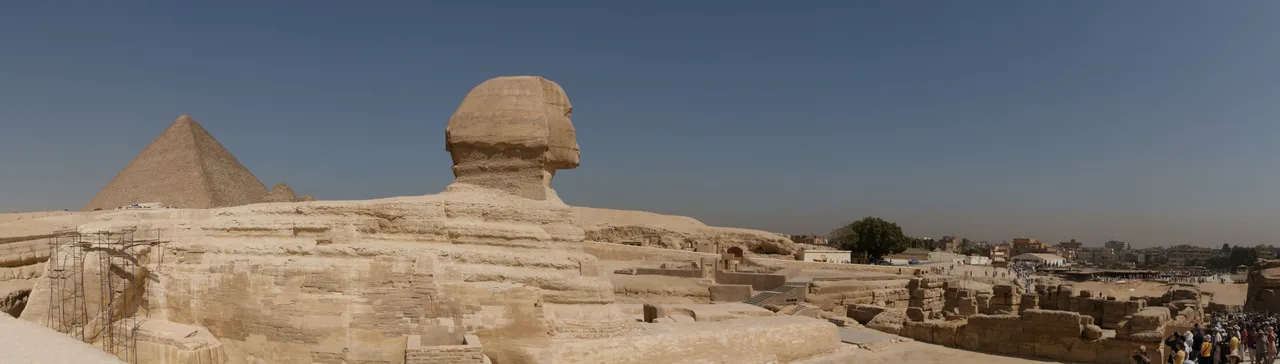 Önde Büyük Sfenks'in geniş heykeli, arkasında çöl üzerinde yükselen Giza piramitlerinin panoramik görüntüsü