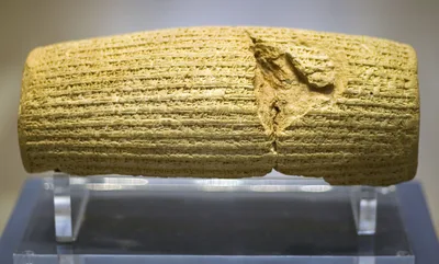 Front view of the Cyrus Cylinder: a barrel-shaped clay artefact covered in cuneiform inscription, partly broken