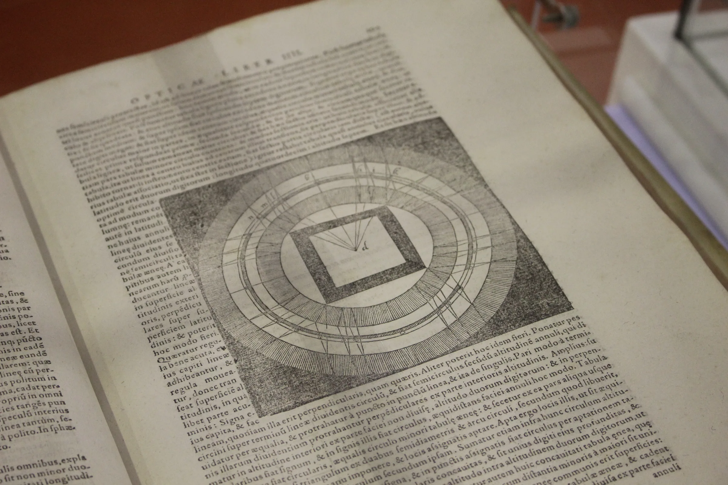 A 1572 edition of Kitab al-Manazir lying open in a display case at a book fair: two pages visible, early typography, leather binding