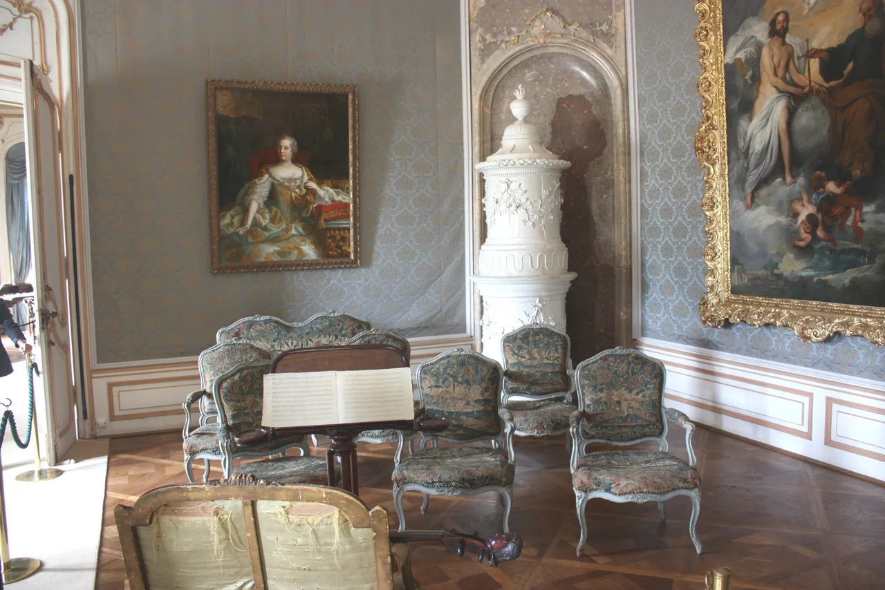 The music salon at Esterháza Palace: gilded wall decoration, crystal chandeliers, white panelling, and a keyboard instrument at the centre