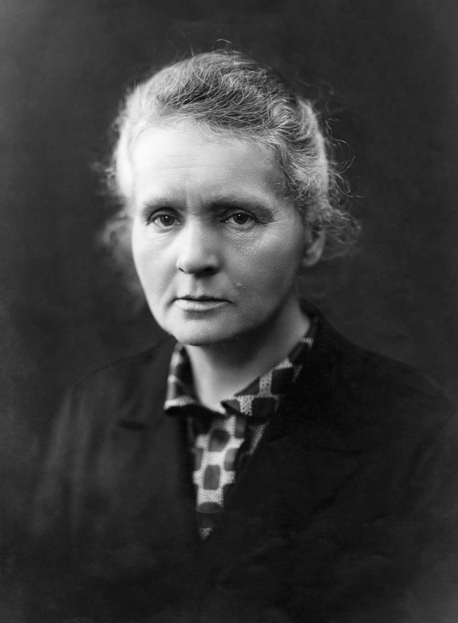 Marie Curie'nin 1920'ler civarında çekilmiş portresi: koyu giysili, ciddi ifadeli orta yaşlı bir kadın