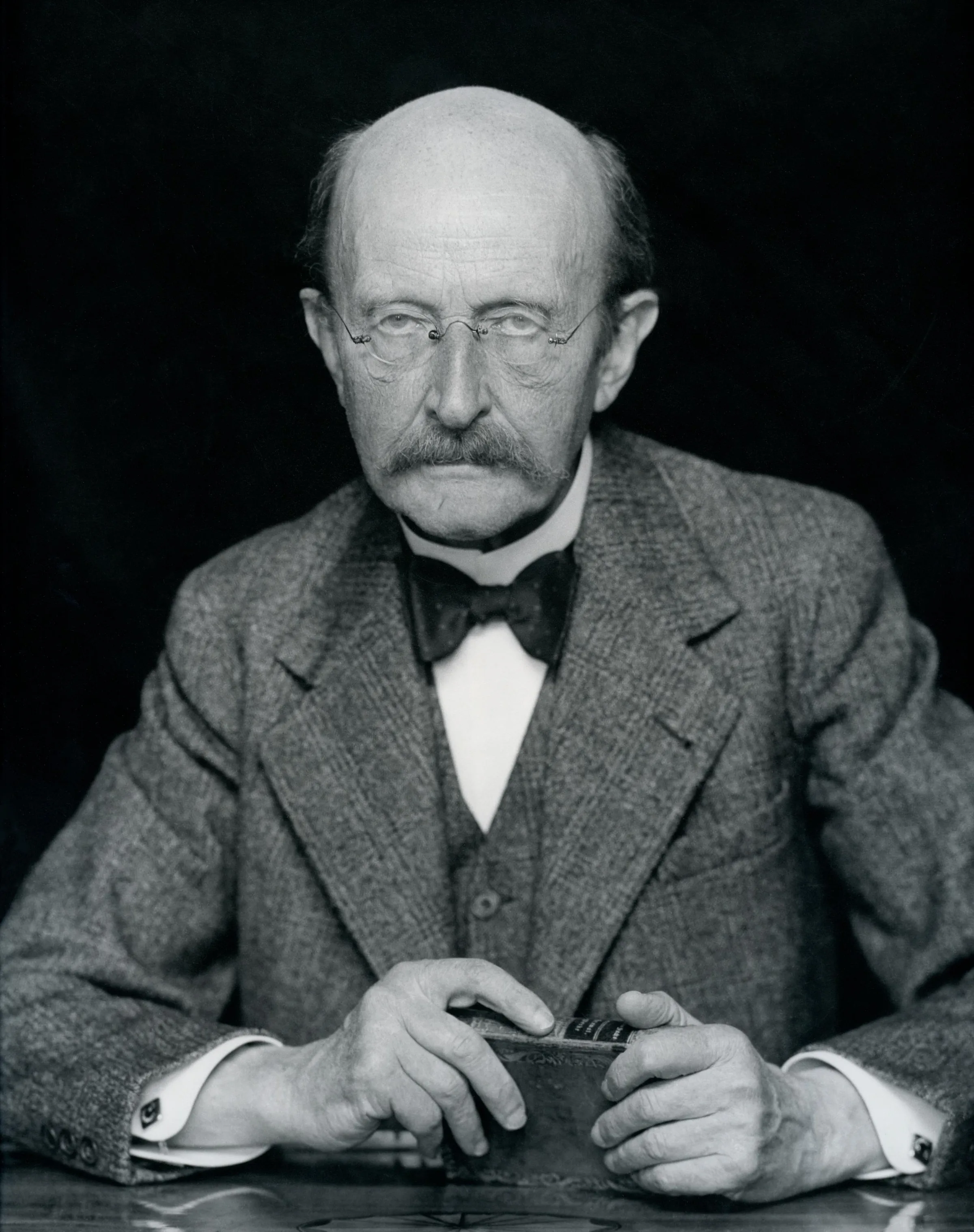 Max Planck'ın 1938 tarihli portresi: gözlüklü, takım elbiseli, kel kafalı yaşlı bir bilim insanı doğrudan kameraya bakıyor
