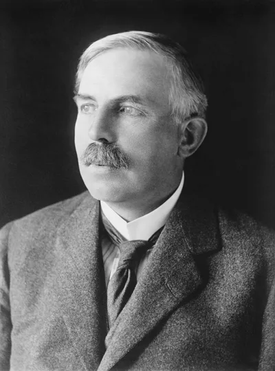A portrait photograph of Ernest Rutherford: a man with a moustache in a dark suit and a serious gaze
