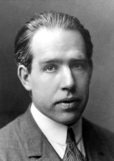 A portrait photograph of Niels Bohr: a young man with hair combed back in a dark suit