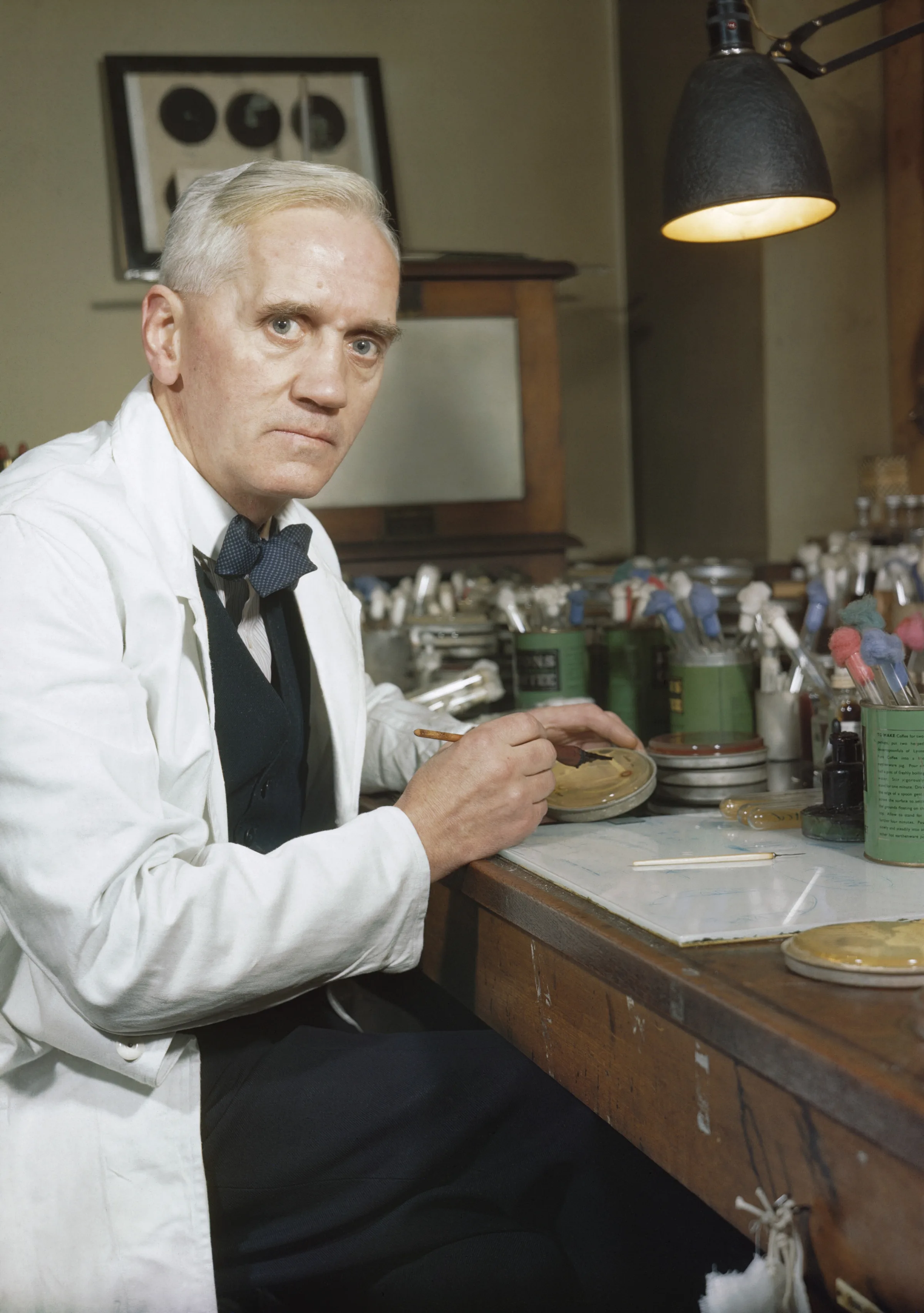 1940s penicillin production facility: a technician in a lab coat checks large glass fermentation vessels