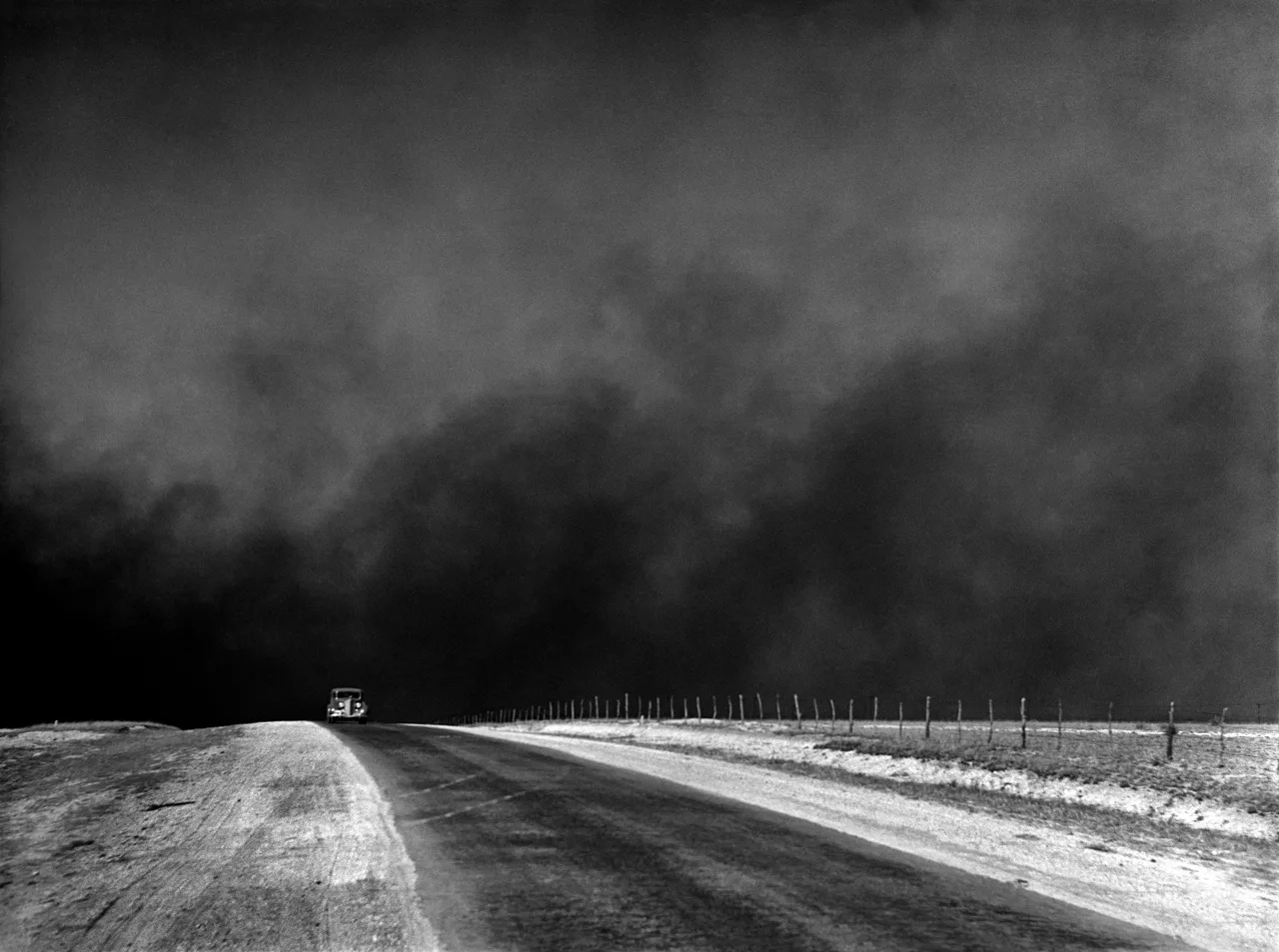 March 1936, Texas Panhandle: a car on a road with heavy clouds of dust rising overhead (the Dust Bowl)