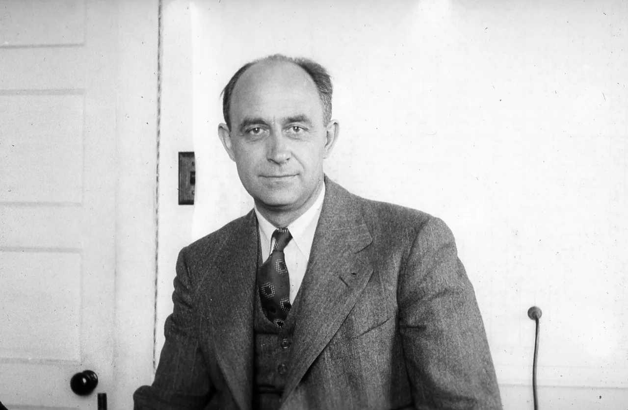 An informal black-and-white portrait of Enrico Fermi: a middle-aged Italian physicist in a white shirt, smiling, looking obliquely at the camera
