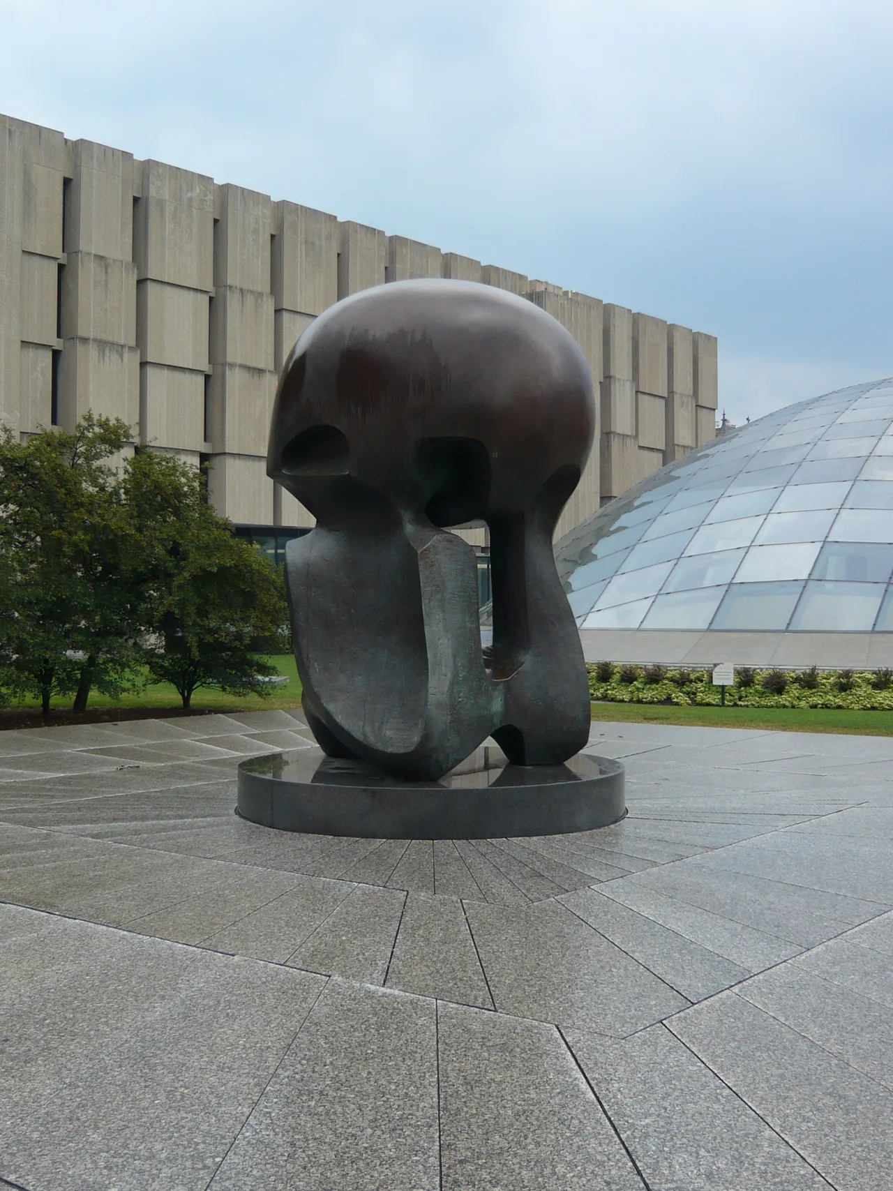 Henry Moore's bronze "Nuclear Energy" sculpture: a spherical mass below, with an upper form that simultaneously suggests a human skull and a mushroom cloud; the University of Chicago campus behind it