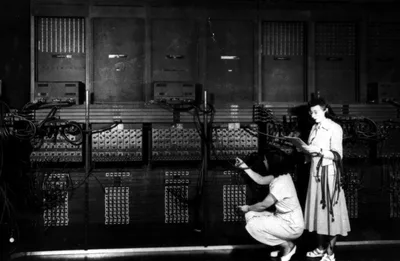Two women rearranging ENIAC's cable panels, with racks of vacuum tubes covering the wall behind