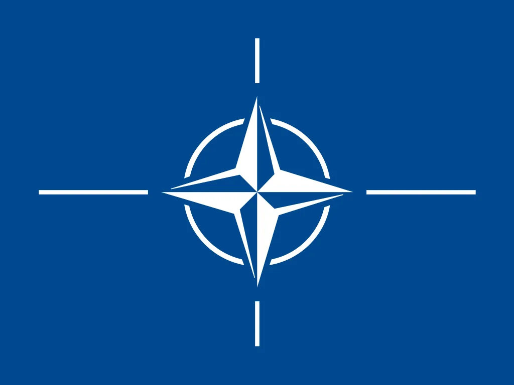 Lacivert zemin üzerinde beyaz dört kollu pusula yıldızı; uçlardan dış halkaya uzanan dört çizgi — NATO bayrağı