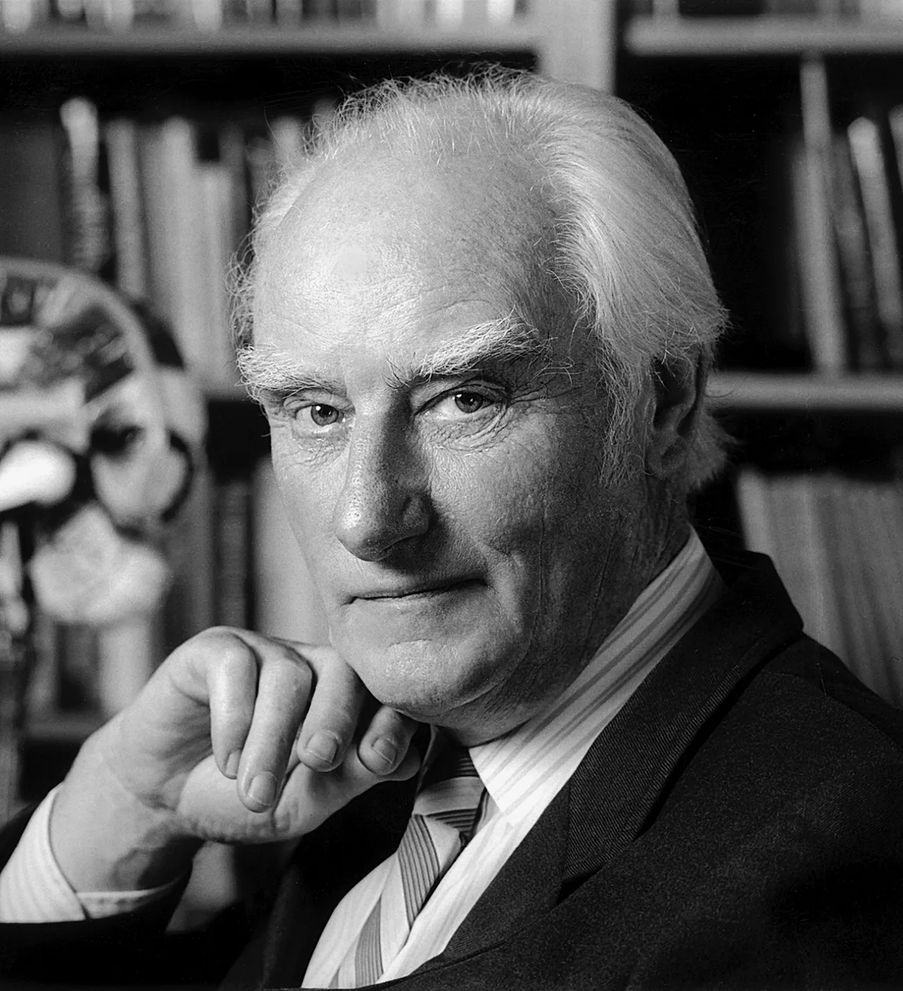 Lab photograph of Francis Crick: a middle-aged man in a suit and glasses, smiling slightly, working with pen and paper