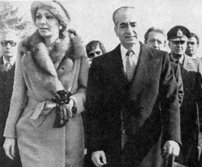 16 Ocak 1979 tarihli fotoğraf: Mehrabad havalimanında Şah Muhammed Rıza Pehlevi koyu paltosuyla, yanında kürk yakalı paltosuyla eşi Farah Pehlevi; ikisi de ciddi ve gerilmiş ifadeyle ileri bakıyor