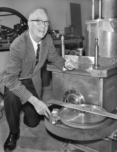 A photograph of Luis Alvarez beside a detector in a laboratory: a scientist in glasses and a suit