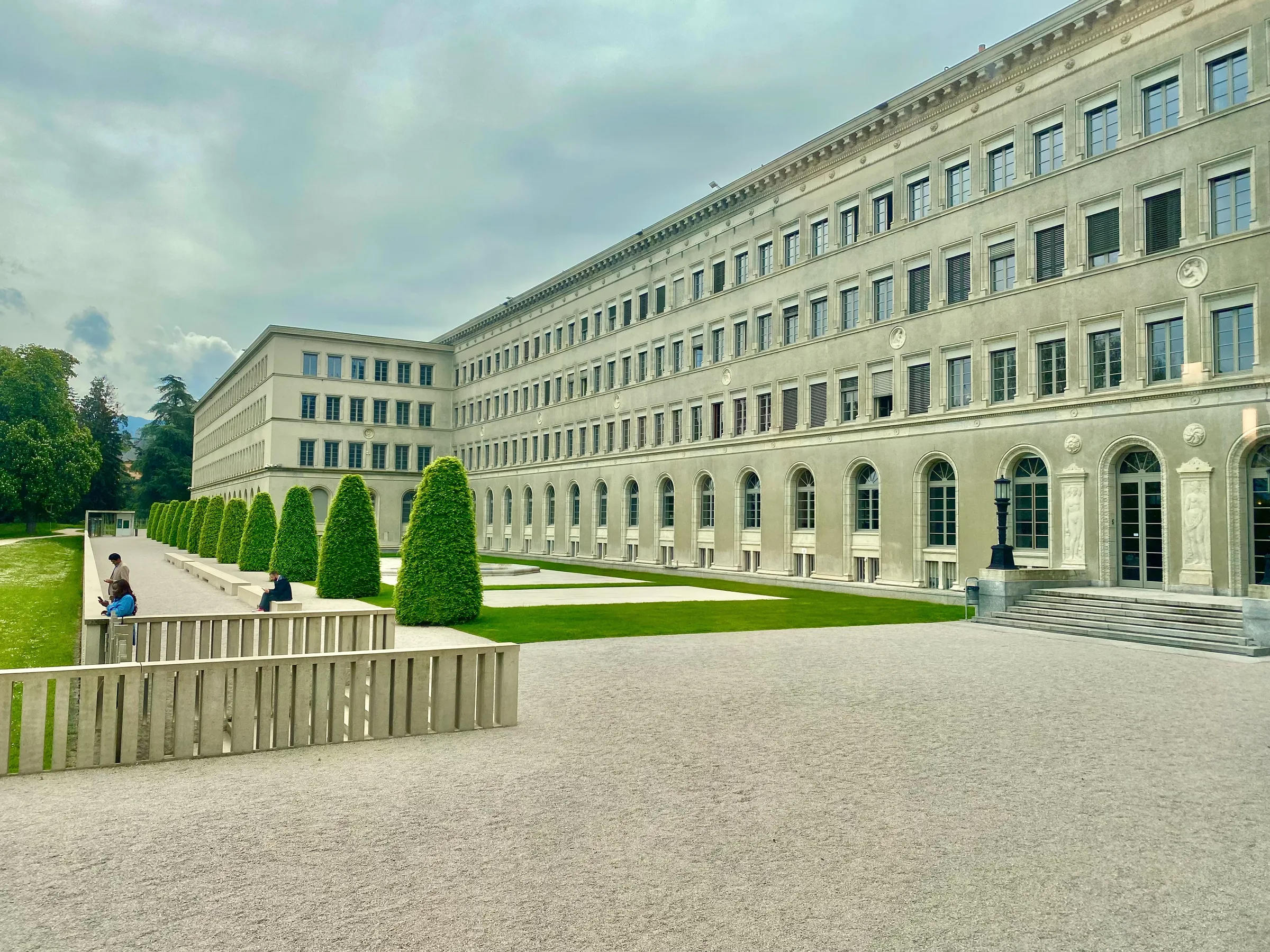 Exterior of the Centre William-Rappard in Geneva: a three-storey early 20th-century stone building with arched windows overlooking Lake Geneva — the headquarters of the WTO