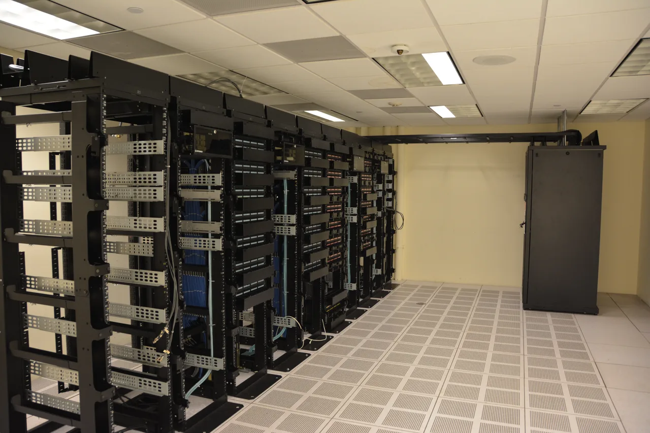 Rows of server racks lit by blue LEDs lining a long corridor in a data centre; the floor is reflective and most of the cabling is hidden.