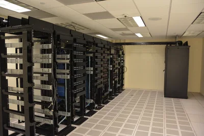 Rows of server racks lit by blue LEDs lining a long corridor in a data centre; the floor is reflective and most of the cabling is hidden.