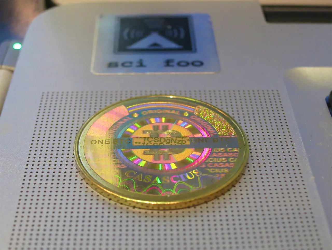 A physical brass Casascius coin engraved with the Bitcoin emblem (a stylised B) and sealed over its private key with a hologram — a single coin on a dark surface