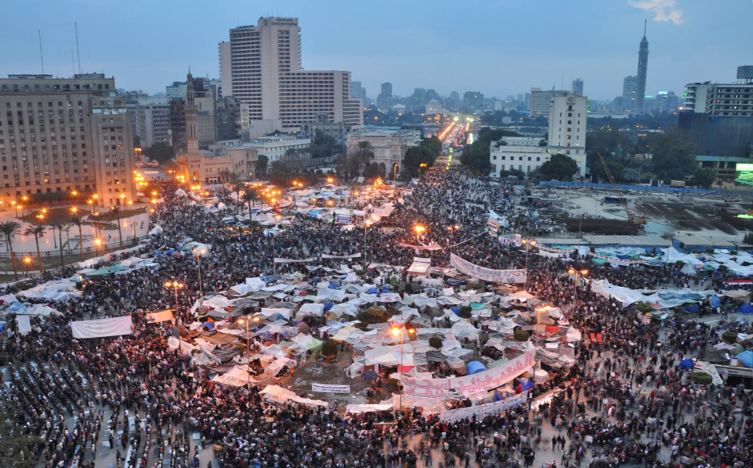 Kahire Tahrir Meydanı'nda yüksek bir noktadan çekilmiş geniş açılı fotoğraf: meydan ve çevresindeki bulvarlar yüz binlerce protestocuyla dolu, ortada büyük bir Mısır bayrağı dalgalanıyor