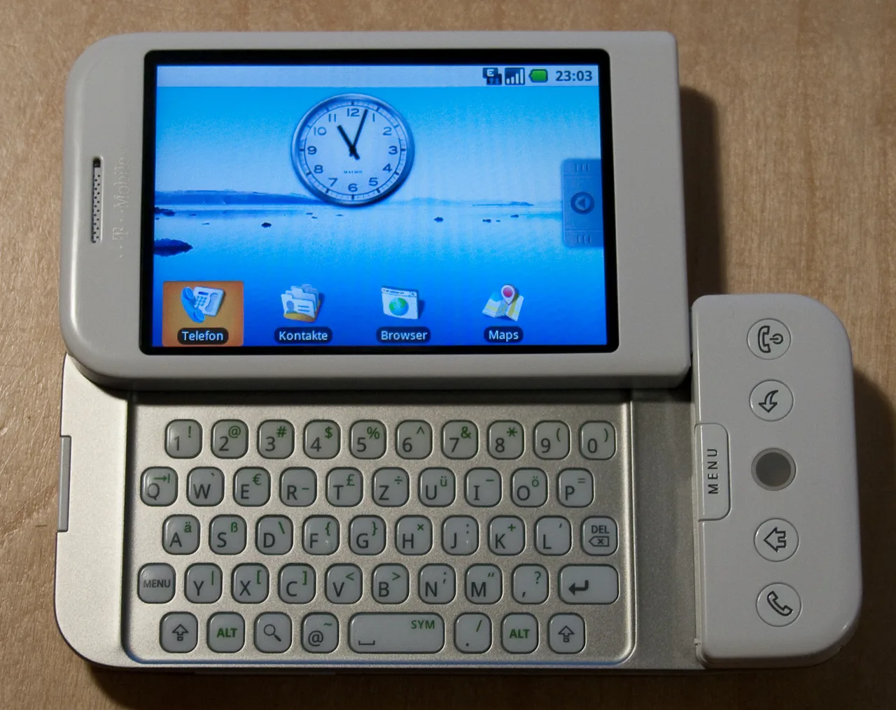 HTC Dream (T-Mobile G1) telefonun ekranı kaydırılarak QWERTY klavyesinin açıldığı görüntü; gümüş gövde, dokunmatik ekran, iz topu (trackball) altta.