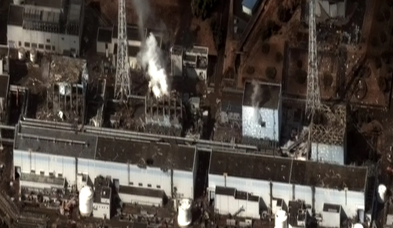 Satellite aerial view of the Fukushima Daiichi plant: of four reactor buildings lined along the coast, three have their roofs blown apart by explosions, with debris scattered around