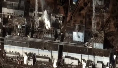 Satellite aerial view of the Fukushima Daiichi plant: of four reactor buildings lined along the coast, three have their roofs blown apart by explosions, with debris scattered around
