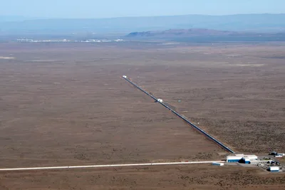 Aerial view of the LIGO Hanford observatory: two long concrete arms branching at right angles across desert terrain, each 4 km long