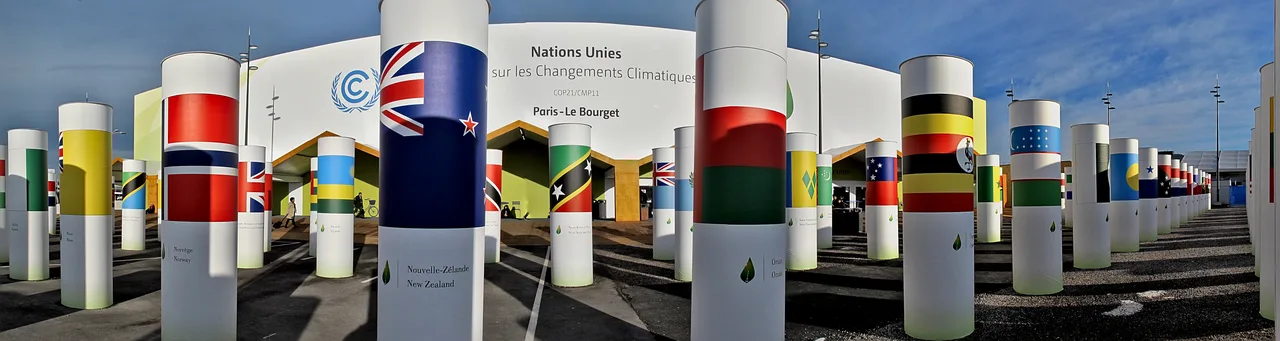Le Bourget'deki COP21 konferans merkezi içinden panoramik görünüm: yüksek tavanlı, mavi ışıklı bir koridor ve katılımcılar