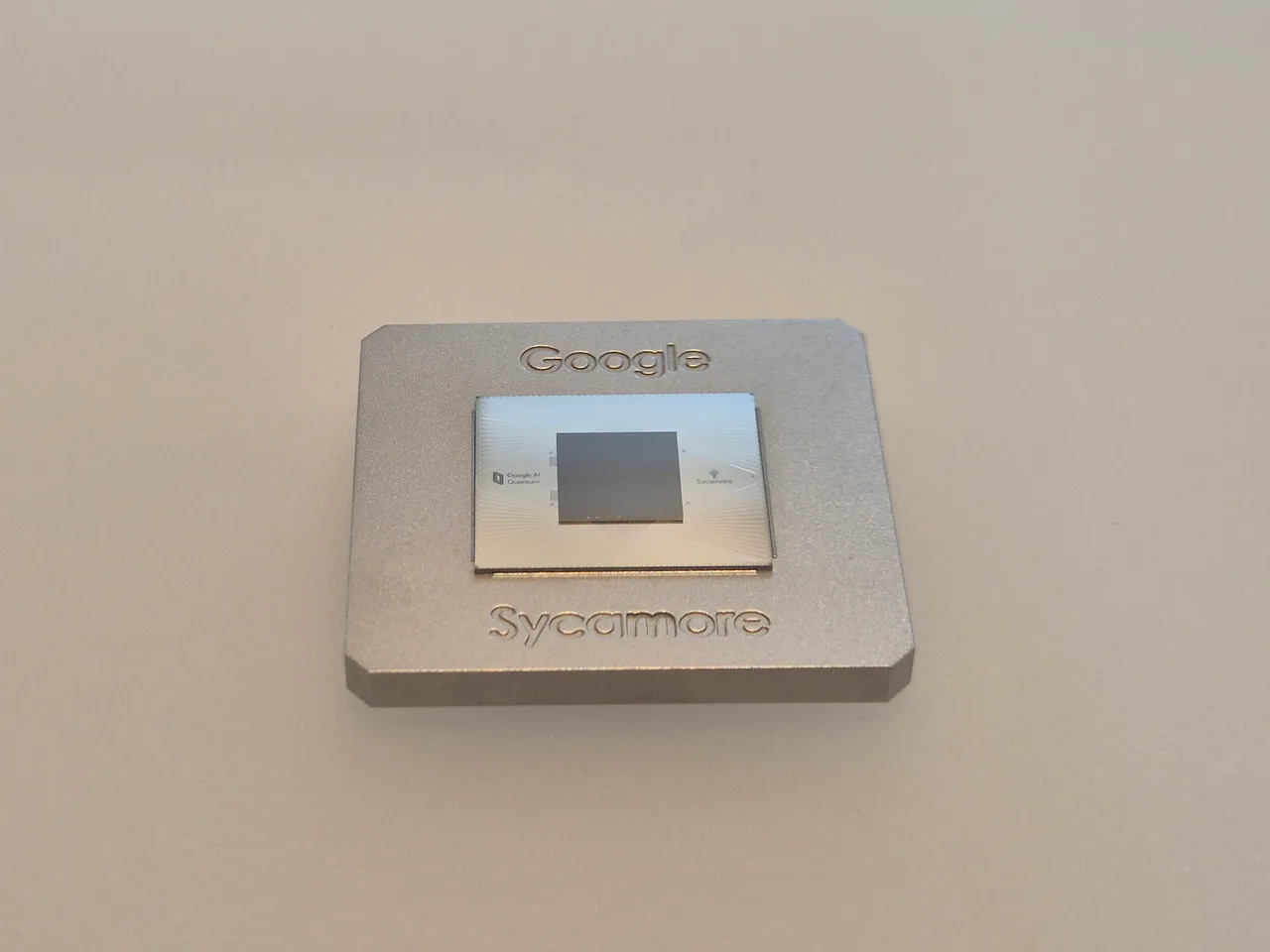 Close-up of the Google Sycamore quantum processor: a small chip on a square gold-coloured metal carrier with fine electronic connectors