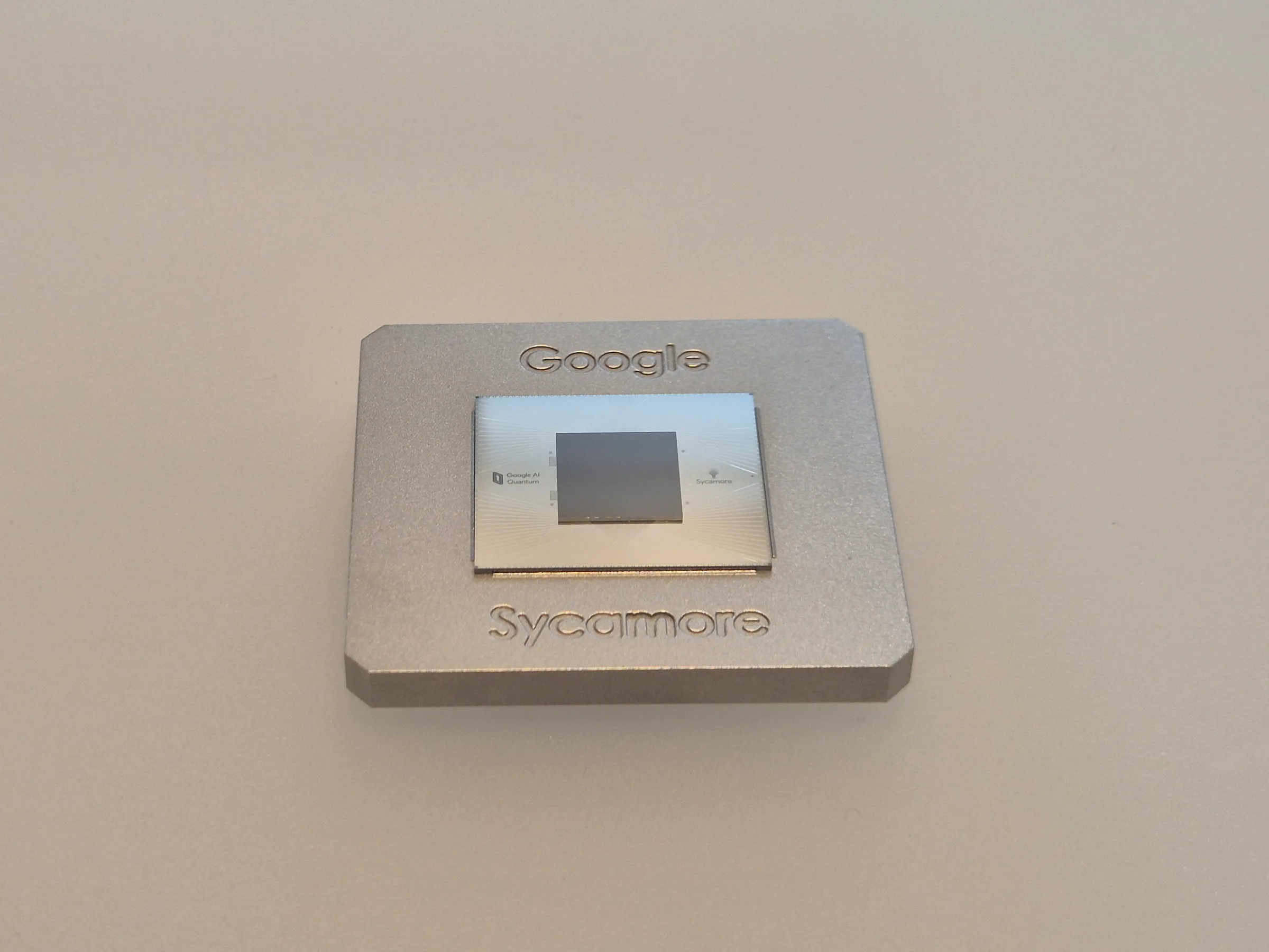 Close-up of the Google Sycamore quantum processor: a small chip on a square gold-coloured metal carrier with fine electronic connectors