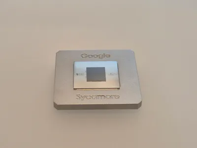 Close-up of the Google Sycamore quantum processor: a small chip on a square gold-coloured metal carrier with fine electronic connectors