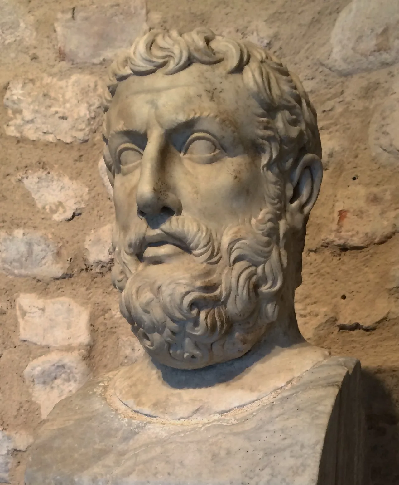 A weathered ancient marble bust of a bearded man at the Velia (Elea) Archaeological Park, identified as Parmenides