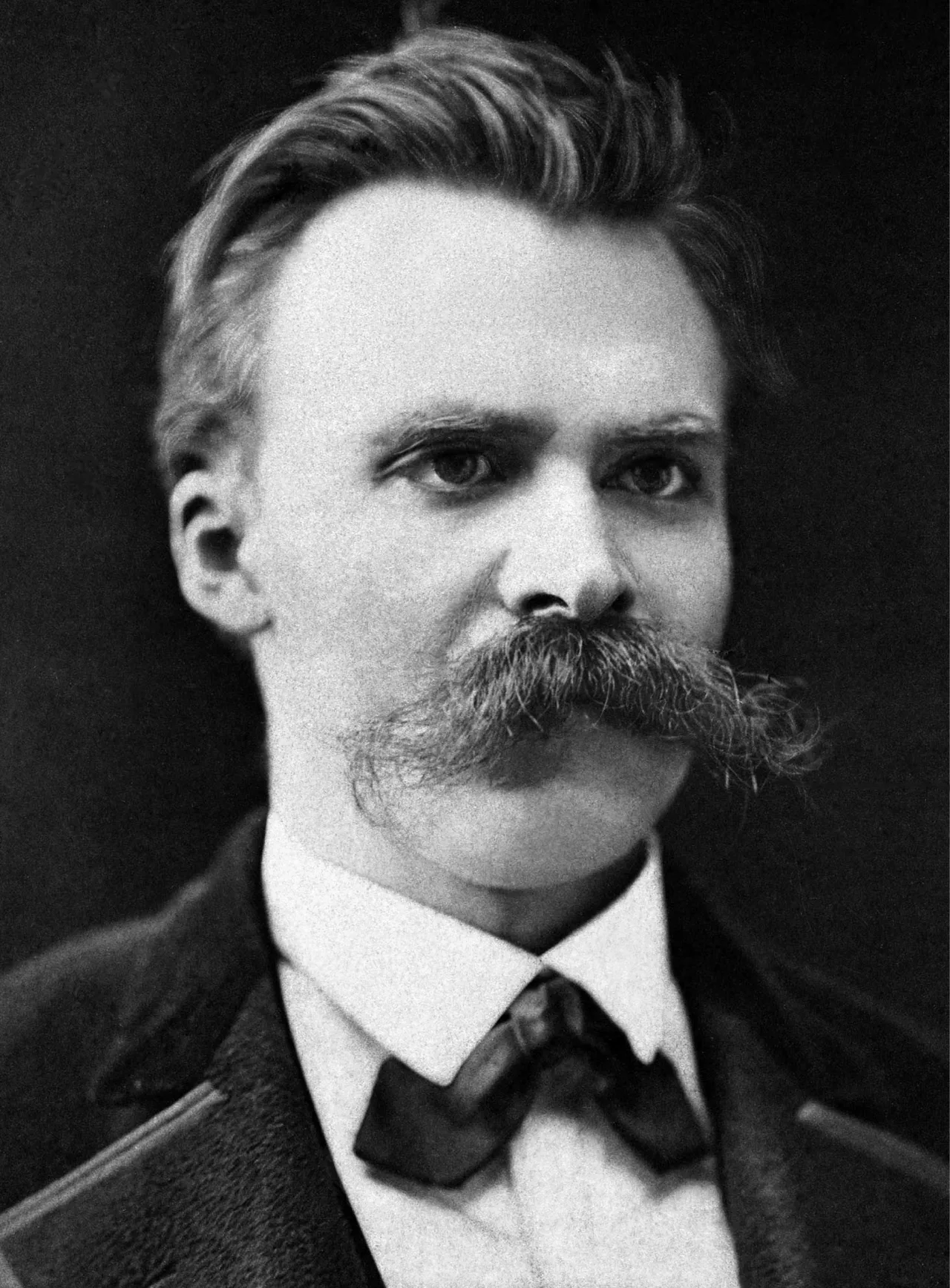 Photograph of Nietzsche, c. 1875: a dark-clothed, moustachioed young philosopher amid many papers