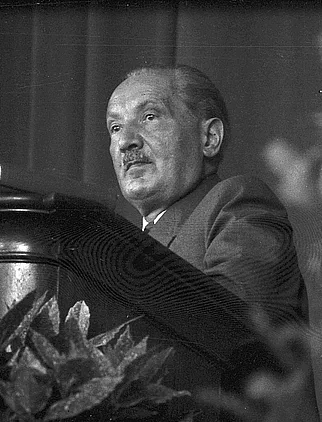 Photograph of Martin Heidegger at a lecture in Freiburg: elderly, balding, in a suit, turned toward an audience