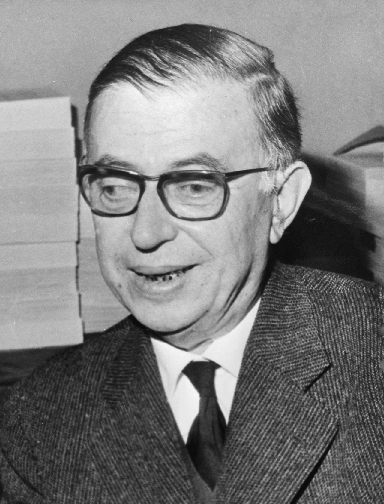 Photograph of Jean-Paul Sartre, 1965: a thinker wearing thick glasses, smoking, turned toward a listener